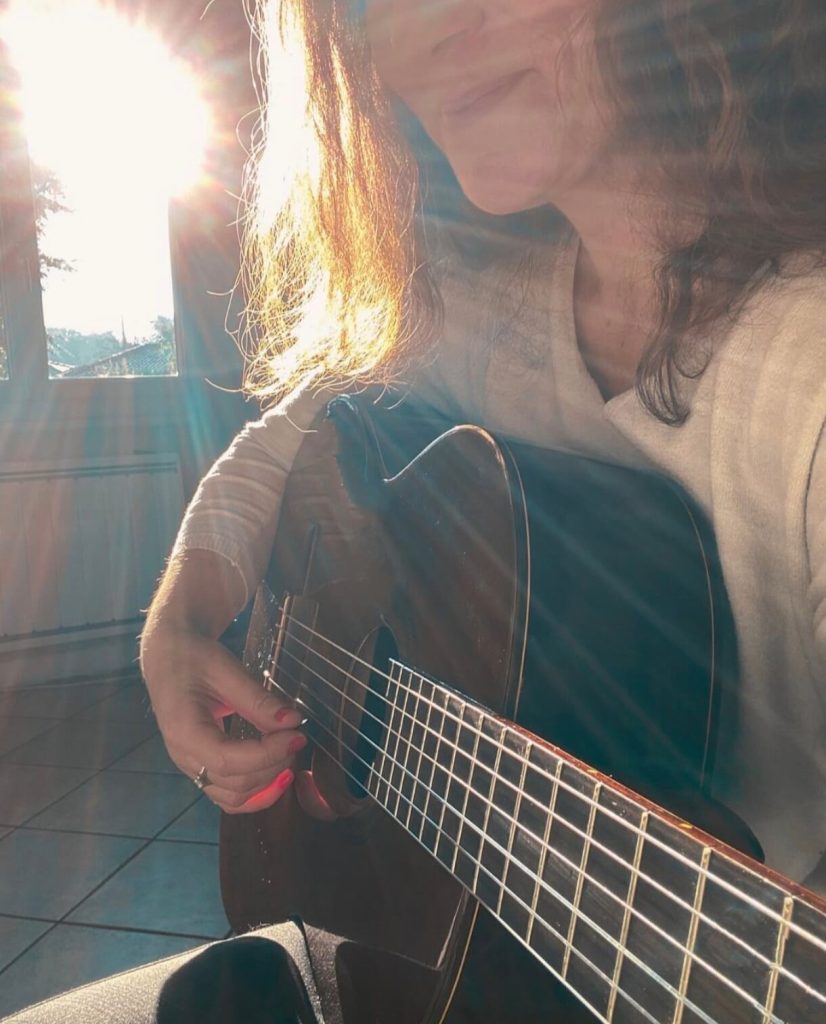 Anne, élève de Guitar Reboot, jouant avec plaisir de sa guitare acoustique, baignée dans la lumière du soleil.